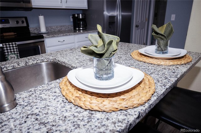 interior details featuring a breakfast bar area, stainless steel range with electric cooktop, white cabinetry, light stone counters, and refrigerator with ice dispenser