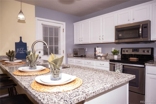 kitchen with appliances with stainless steel finishes, white cabinetry, hanging light fixtures, a center island, and light stone counters