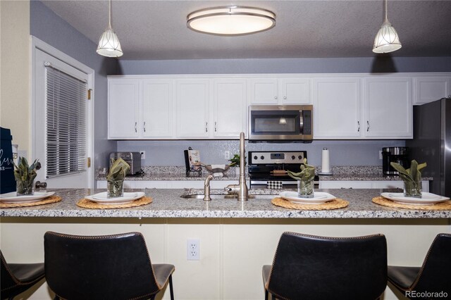 kitchen with stainless steel appliances, hanging light fixtures, and white cabinets