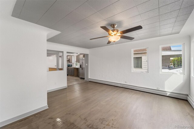 unfurnished living room with ceiling fan, a baseboard radiator, and wood-type flooring