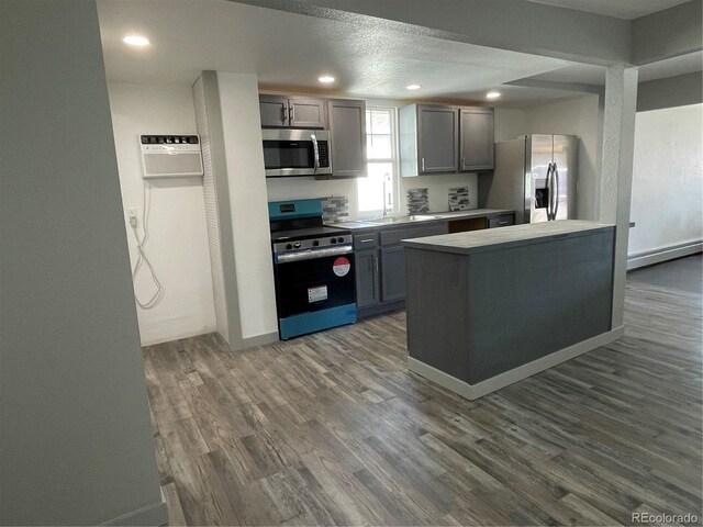 kitchen featuring gray cabinetry, a wall mounted AC, dark hardwood / wood-style flooring, stainless steel appliances, and a textured ceiling