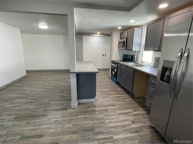 kitchen with sink, appliances with stainless steel finishes, a textured ceiling, a kitchen island, and dark hardwood / wood-style flooring