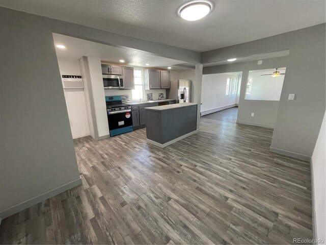 kitchen with stainless steel appliances, a baseboard heating unit, gray cabinetry, and dark hardwood / wood-style flooring