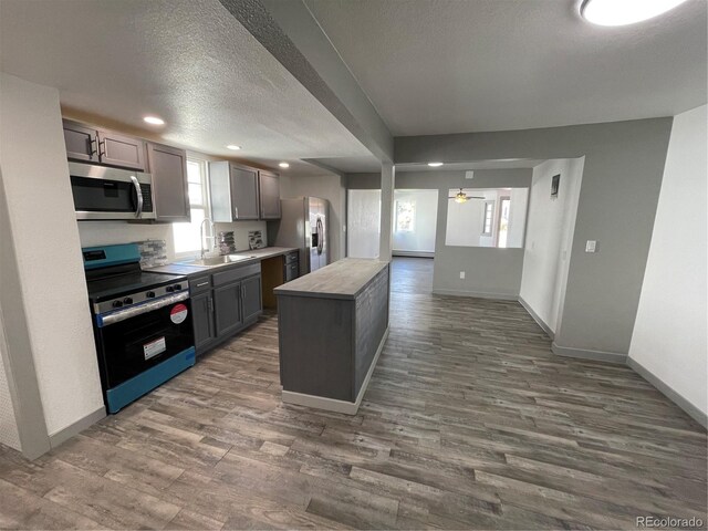 kitchen with dark wood-type flooring, sink, a textured ceiling, a kitchen island, and stainless steel appliances