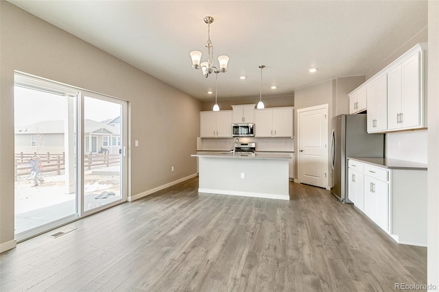 kitchen featuring white cabinetry, hanging light fixtures, light hardwood / wood-style flooring, an island with sink, and appliances with stainless steel finishes