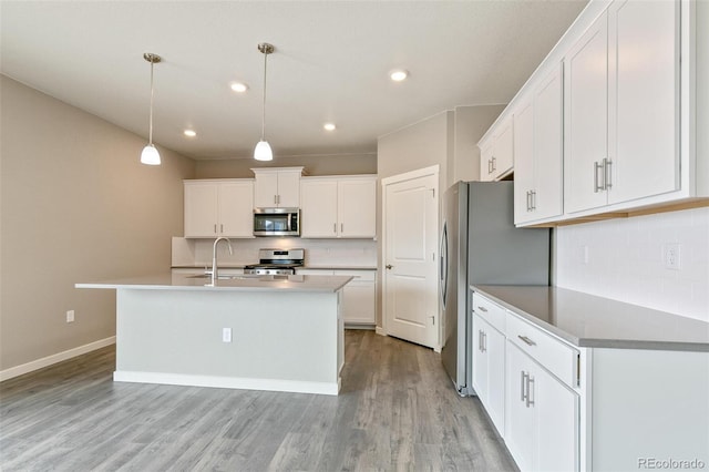 kitchen with pendant lighting, light wood-type flooring, an island with sink, appliances with stainless steel finishes, and white cabinetry