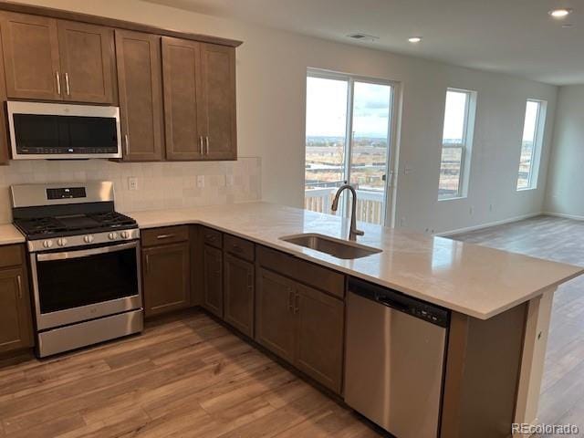 kitchen with kitchen peninsula, stainless steel appliances, sink, and light wood-type flooring