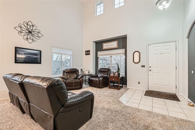 living area with a high ceiling, light carpet, baseboards, and light tile patterned floors