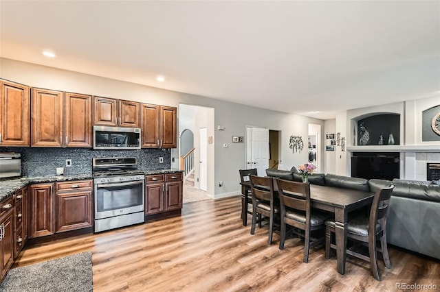 kitchen featuring light wood finished floors, stainless steel appliances, tasteful backsplash, a tiled fireplace, and open floor plan