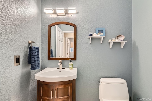 half bathroom with toilet, a textured wall, and vanity