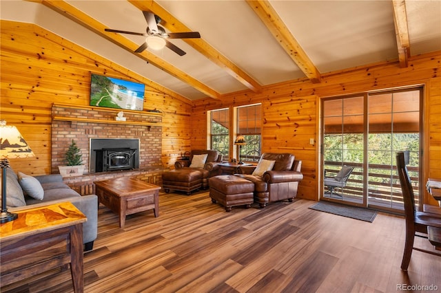 living room with ceiling fan, wood walls, a brick fireplace, hardwood / wood-style flooring, and lofted ceiling with beams