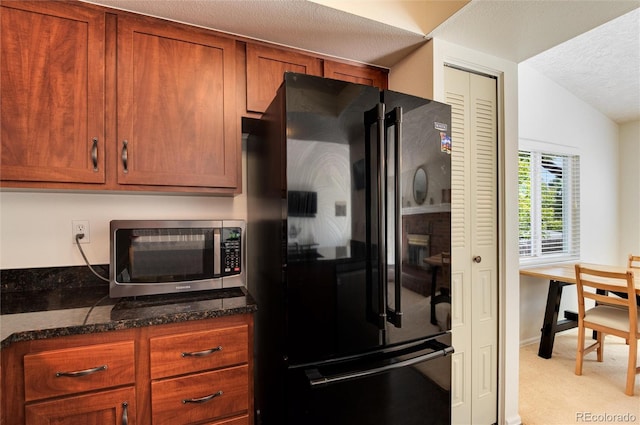 kitchen with lofted ceiling, black fridge, light carpet, dark stone counters, and a textured ceiling