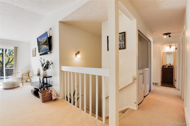 hallway featuring independent washer and dryer, a textured ceiling, and light colored carpet