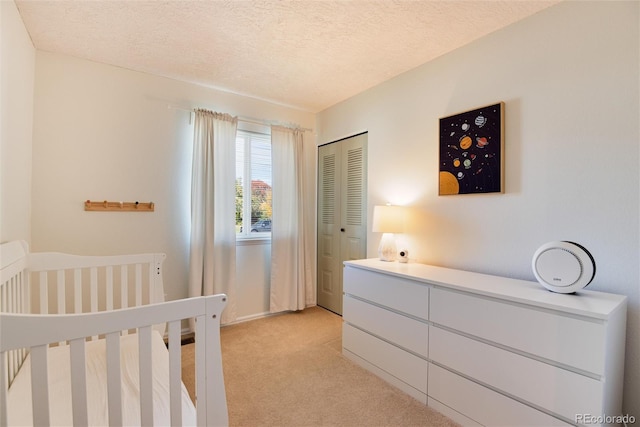 carpeted bedroom featuring a nursery area, a textured ceiling, and a closet