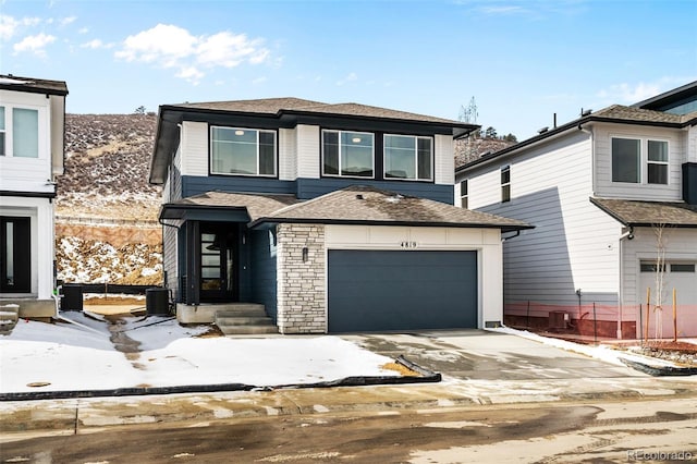 prairie-style home featuring central AC unit, stone siding, an attached garage, and concrete driveway