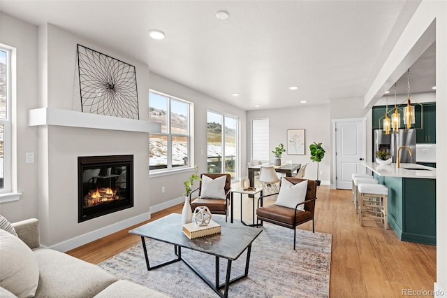 living room featuring baseboards, light wood finished floors, a glass covered fireplace, and recessed lighting