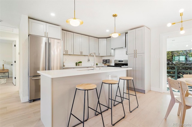 kitchen with sink, decorative light fixtures, a center island with sink, appliances with stainless steel finishes, and light wood-type flooring