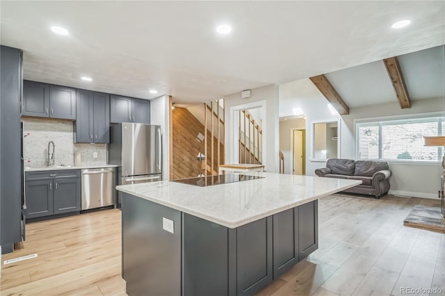 kitchen featuring decorative backsplash, light wood-style floors, light stone counters, a sink, and appliances with stainless steel finishes