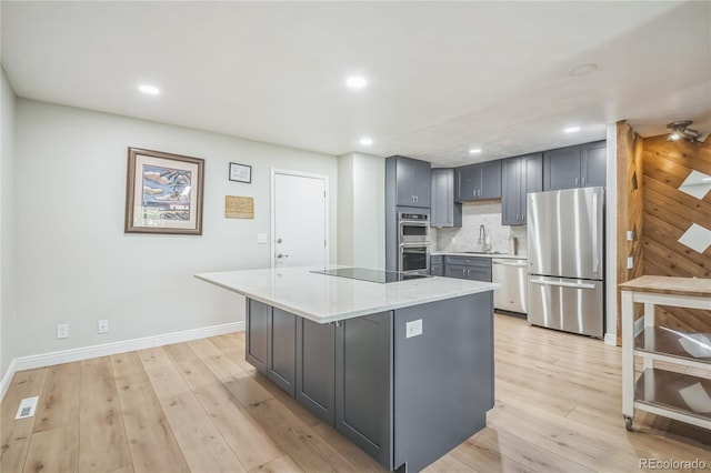 kitchen with light stone counters, a sink, light wood-style flooring, appliances with stainless steel finishes, and gray cabinetry