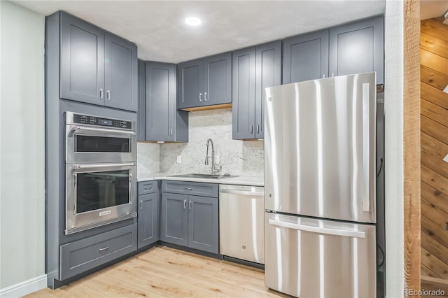 kitchen with gray cabinets, light wood-type flooring, a sink, light countertops, and stainless steel appliances