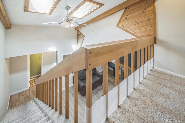 stairway with beamed ceiling, carpet floors, a ceiling fan, baseboards, and a skylight