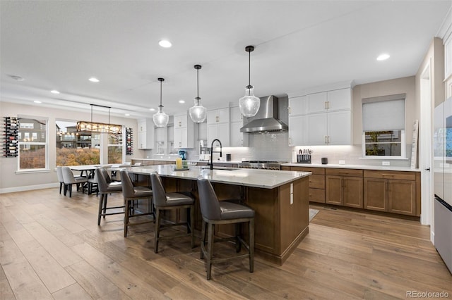 kitchen with light stone counters, wall chimney exhaust hood, white cabinetry, a large island with sink, and sink