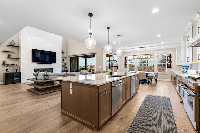 kitchen with a center island with sink, light wood-type flooring, pendant lighting, sink, and white cabinetry