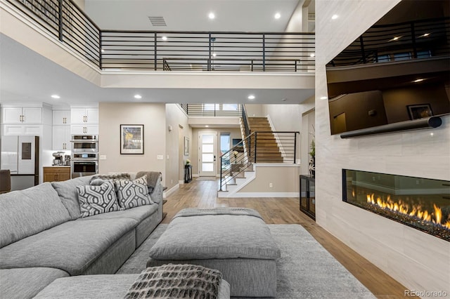 living room featuring a towering ceiling, a tile fireplace, and light hardwood / wood-style floors