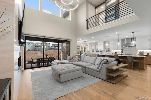 living room with a towering ceiling, sink, a chandelier, and light wood-type flooring