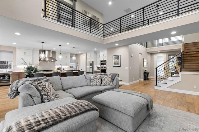 living room featuring a towering ceiling, beverage cooler, sink, and light hardwood / wood-style flooring