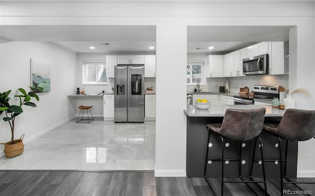 kitchen with kitchen peninsula, a kitchen breakfast bar, appliances with stainless steel finishes, and white cabinetry