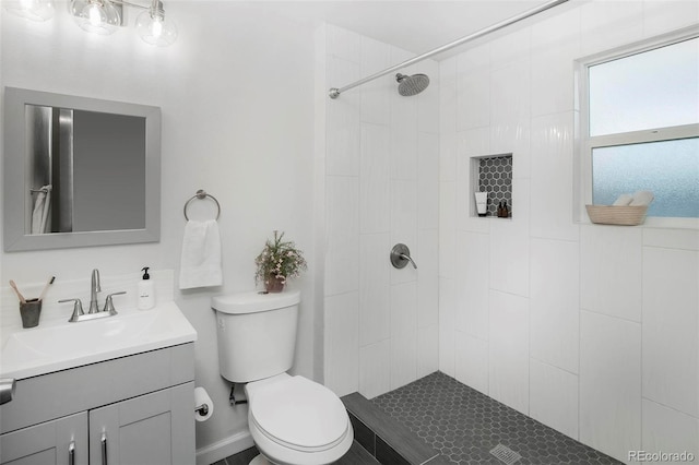 bathroom with toilet, a tile shower, and vanity