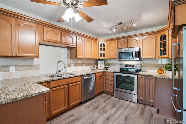 kitchen with sink, light stone counters, a textured ceiling, light hardwood / wood-style floors, and stainless steel appliances