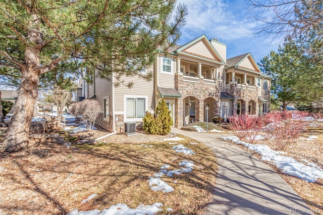 view of front of house with stone siding, a balcony, and central air condition unit