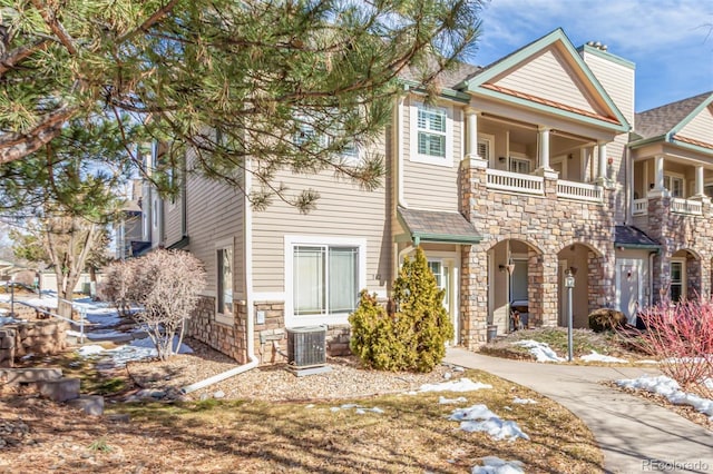 view of front of house featuring stone siding, central AC, a balcony, and roof with shingles