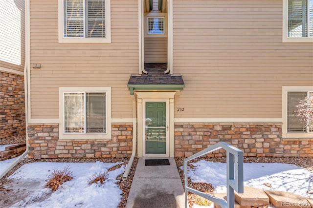 snow covered property entrance with stone siding