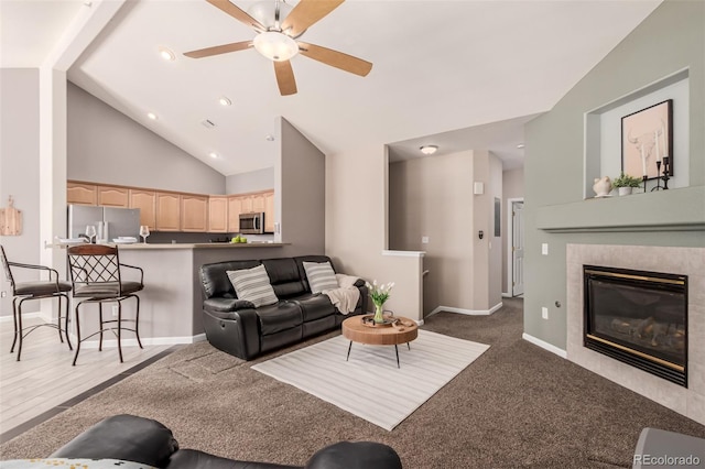 living area featuring baseboards, a ceiling fan, a tile fireplace, dark colored carpet, and high vaulted ceiling