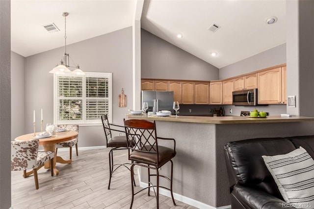 kitchen featuring a breakfast bar area, light brown cabinets, appliances with stainless steel finishes, light wood-type flooring, and decorative light fixtures