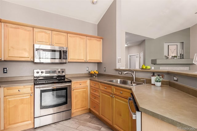 kitchen featuring light brown cabinets, appliances with stainless steel finishes, vaulted ceiling, and a sink