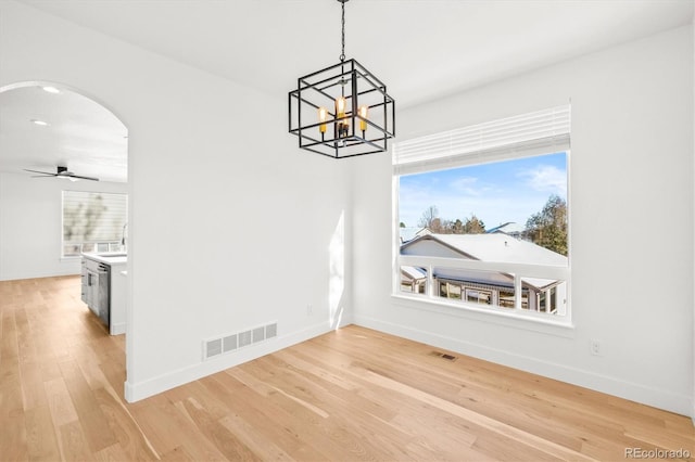 unfurnished dining area with ceiling fan with notable chandelier, light hardwood / wood-style floors, and a wealth of natural light