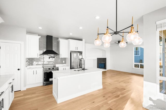 kitchen with appliances with stainless steel finishes, wall chimney range hood, decorative light fixtures, light hardwood / wood-style floors, and white cabinetry