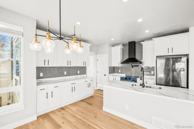 kitchen featuring refrigerator, wall chimney exhaust hood, sink, white cabinetry, and hanging light fixtures