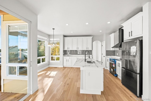 kitchen with white cabinets, black fridge, sink, range with electric cooktop, and wall chimney exhaust hood