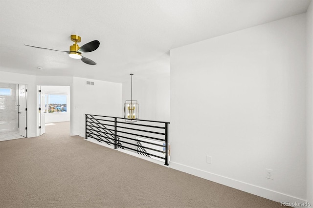 carpeted spare room featuring ceiling fan with notable chandelier