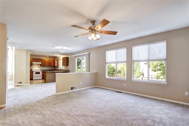 unfurnished living room with ceiling fan, light colored carpet, and sink