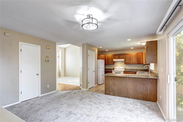 kitchen with white appliances, kitchen peninsula, light colored carpet, and sink