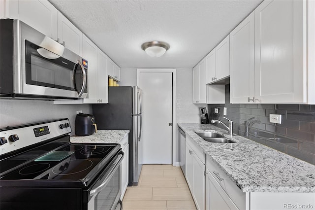 kitchen with stainless steel appliances, a sink, white cabinets, tasteful backsplash, and a textured ceiling