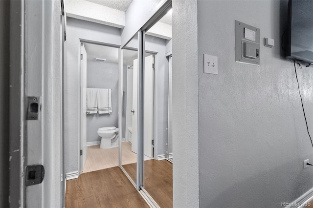 bathroom with wood finished floors, toilet, a textured wall, and baseboards