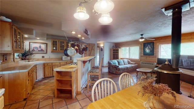 interior space featuring ceiling fan, tile counters, light tile patterned floors, and a wood stove