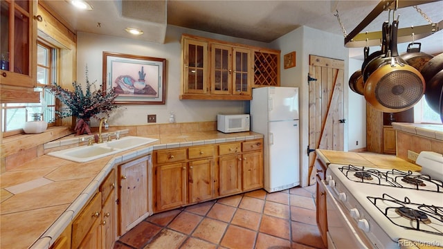 kitchen with light tile patterned floors, tile countertops, white appliances, and sink